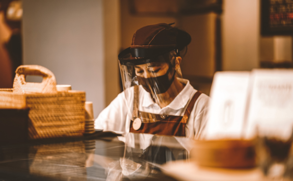 A worker in a cafe wears a face mask and a safety face visor